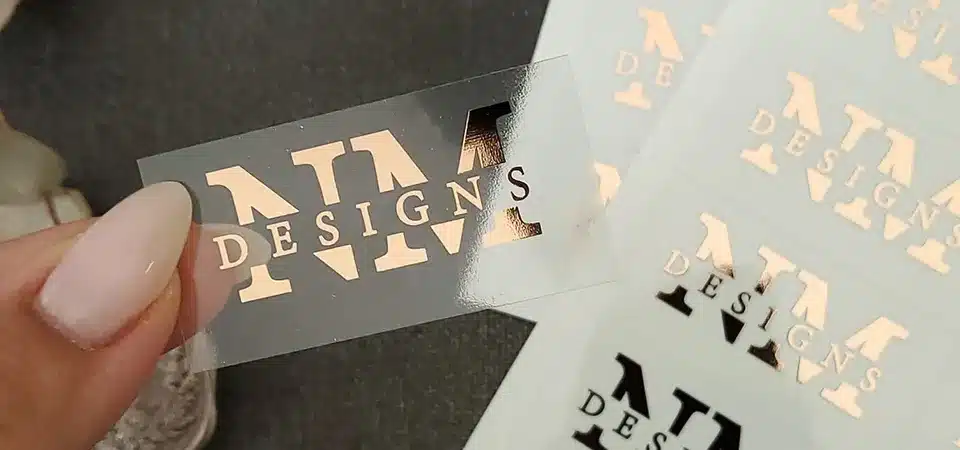A clear sticker with a company logo applied to a glass office door and a metal laptop.