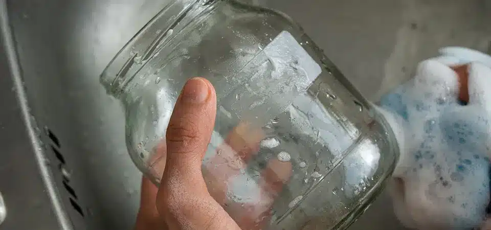 A glass jar soaking in a sink full of sudsy water.