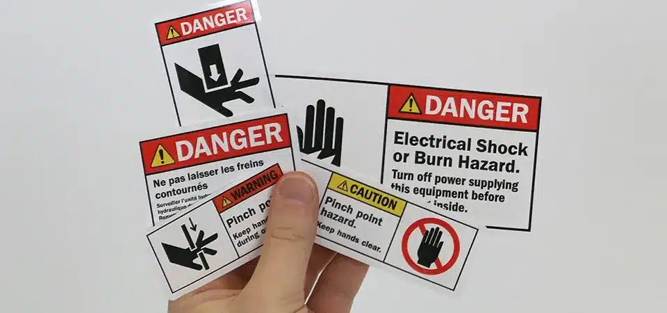 A bright yellow safety warning label from a roll being applied to a piece of machinery.