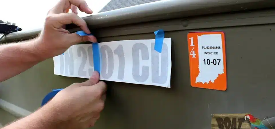A person applying a large boat sticker using the hinge method with masking tape and a squeegee.