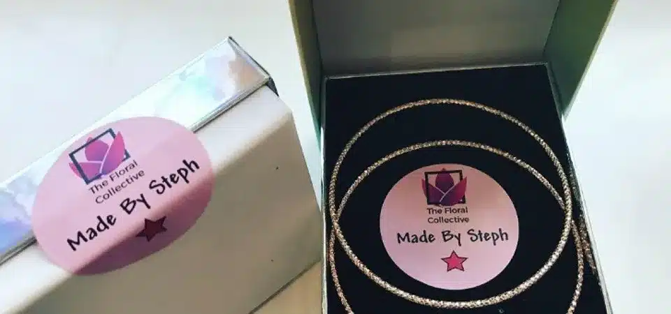 A small, circular branded sticker from a roll being used to seal tissue paper in a gift box.