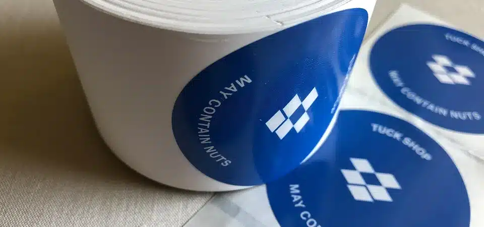 A hand peeling a biodegradable sticker, revealing the shiny, non-compostable backing paper.