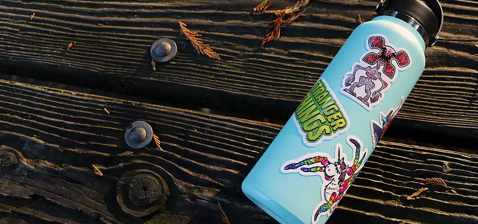 A comparison of three sticker materials: a peeling paper sticker, a standard vinyl sticker, and a durable laminated vinyl sticker.
