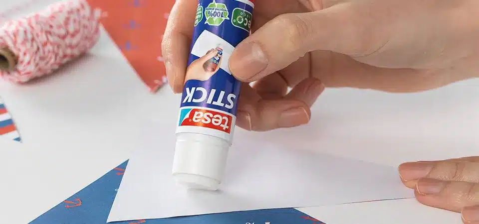A person applying a clear glue stick to the back of a paper sticker