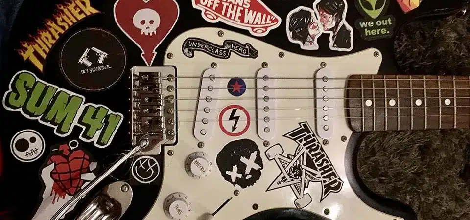 A black hardshell guitar case covered in stickers from bands and music shops