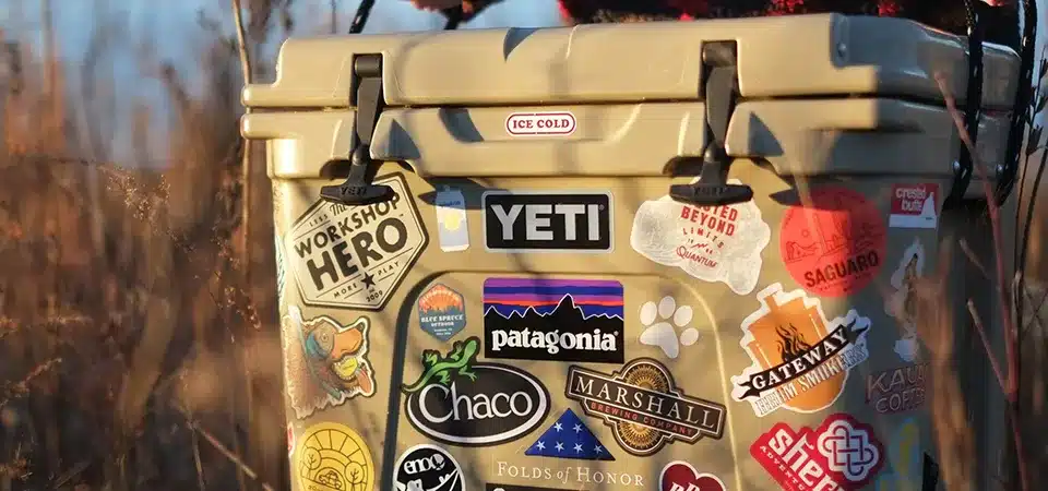 A large cooler completely covered in stickers from breweries, parks, and fishing brands