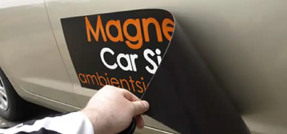 A picture of a weathered car sticker still intact and a magnet that is peeling at the corner