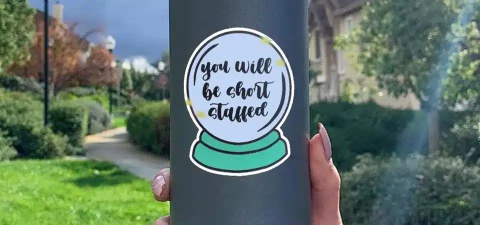 Hands gently washing a sticker-covered water bottle with a soft sponge in a sink