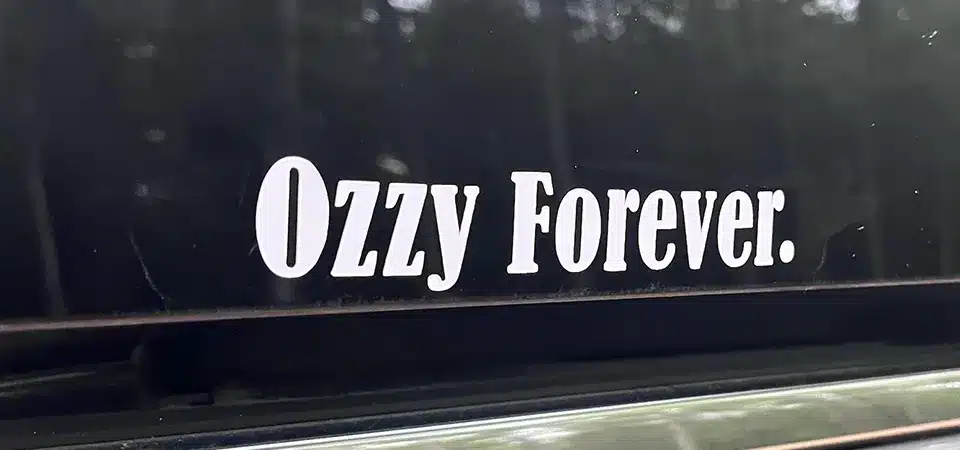 A "For Sale" sign in a car window, with some taste-specific stickers visible on the bumper