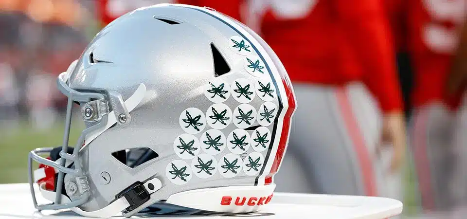 A football team huddled together, their helmets full of stickers shining under the stadium lights