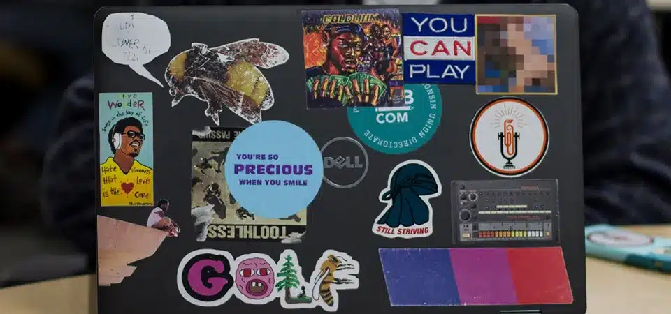 A sticker-covered laptop next to a similarly decorated water bottle on a desk
