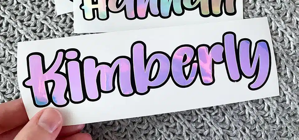A flat-lay of tools for making vinyl stickers: vinyl rolls, a Cricut machine, weeding tools, and transfer tape