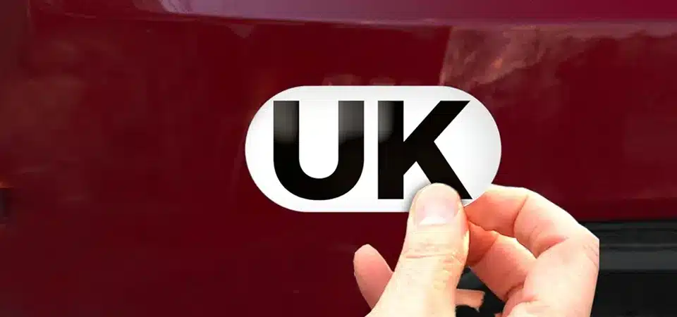 A close-up of a white oval UK car sticker showing the letters clearly