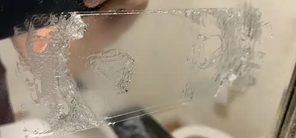 A spray bottle of white vinegar next to a mirror with a sticky residue spot
