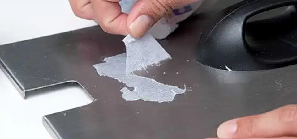 Using soapy water to remove a paper sticker from metal A sponge soaked in soapy water being pressed onto a paper sticker on a metal cabinet
