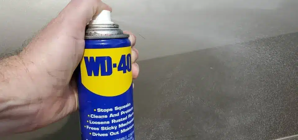 A can of WD-40 being sprayed on a stubborn sticker on a car window