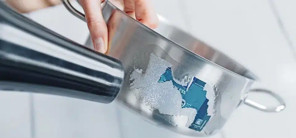 Using baby oil to remove sticker residue from metal A person applying baby oil with a cotton ball to a sticker on a metal laptop lid