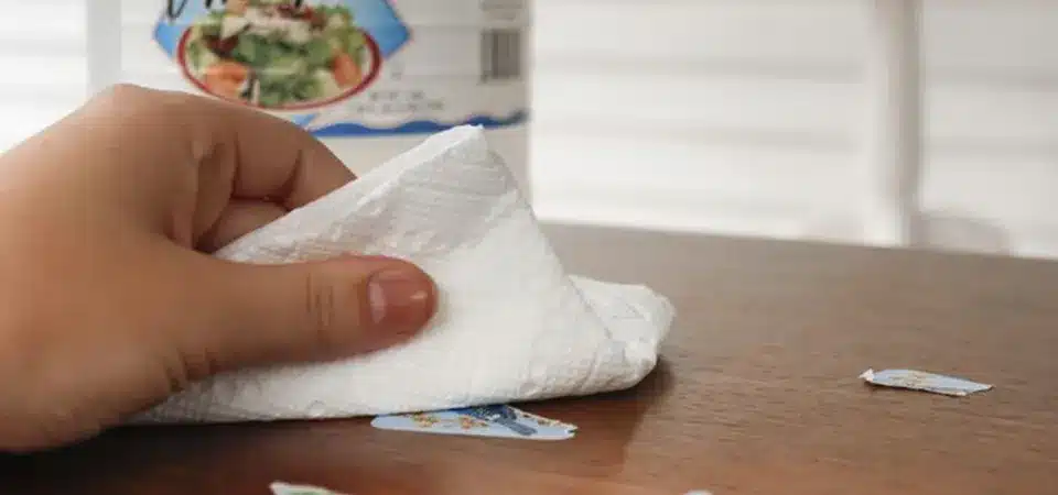 A paper towel soaked in white vinegar placed over a sticker on a wooden floor