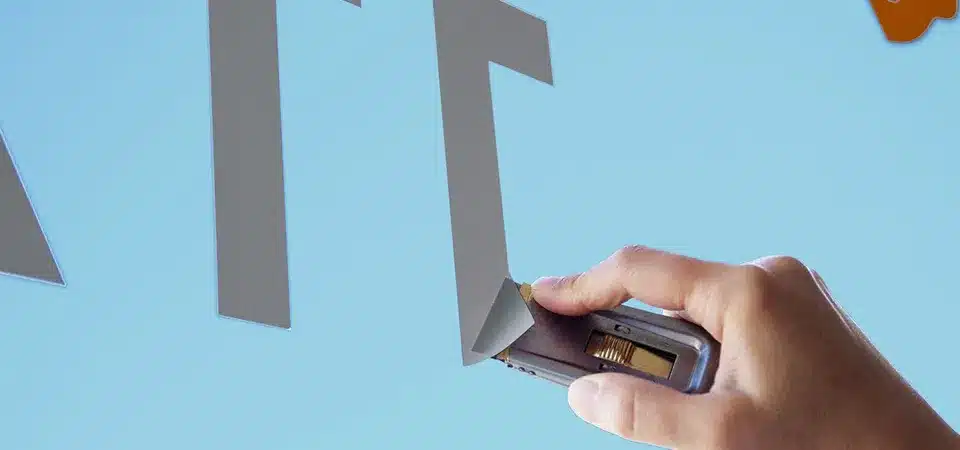 A person carefully using a razor blade scraper at a very low angle to remove tough residue from a mirror