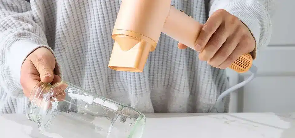 A hair dryer being held several inches away from a mirror to warm a sticker residue spot