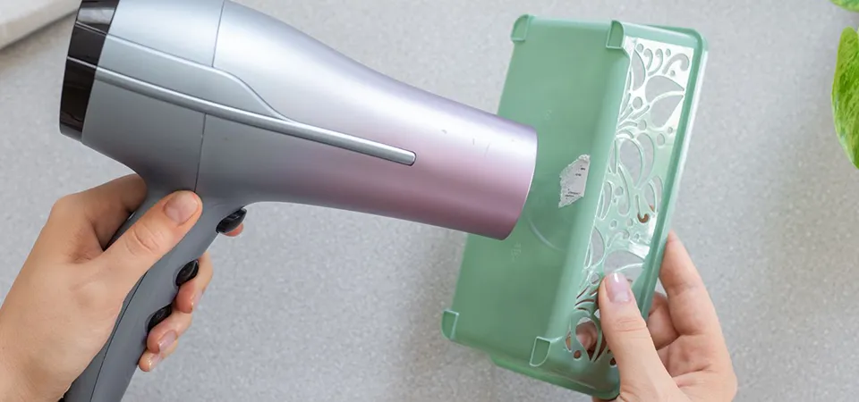 A person using a hairdryer to warm up a sticker on a plastic laptop lid before peeling it