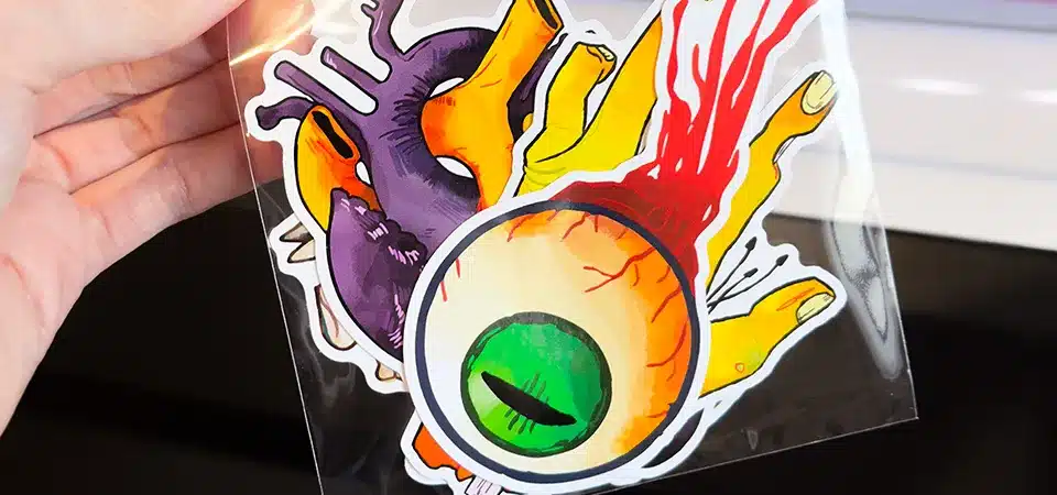 A person decorating their laptop and phone case with stickers from a newly opened pack
