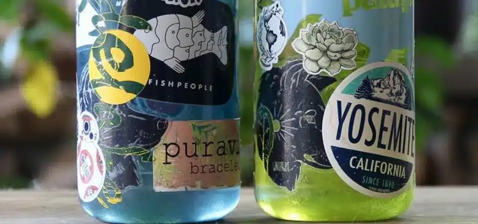 A water bottle covered in stickers resting safely on the top rack of a lit dishwasher