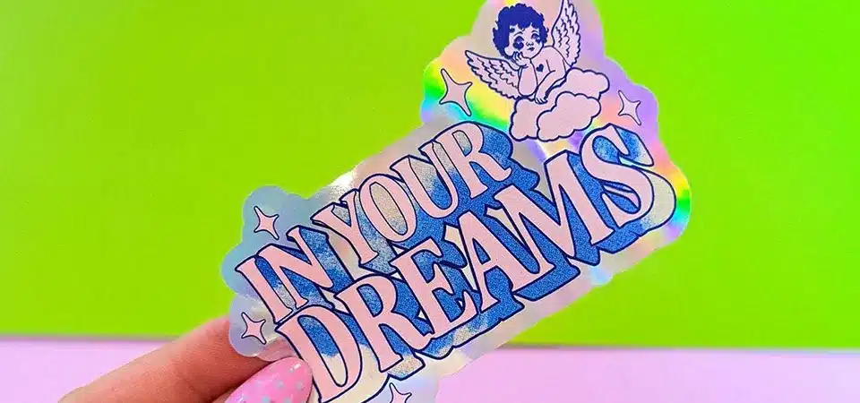 A person holding a physical holographic sticker sample up to the light to inspect it