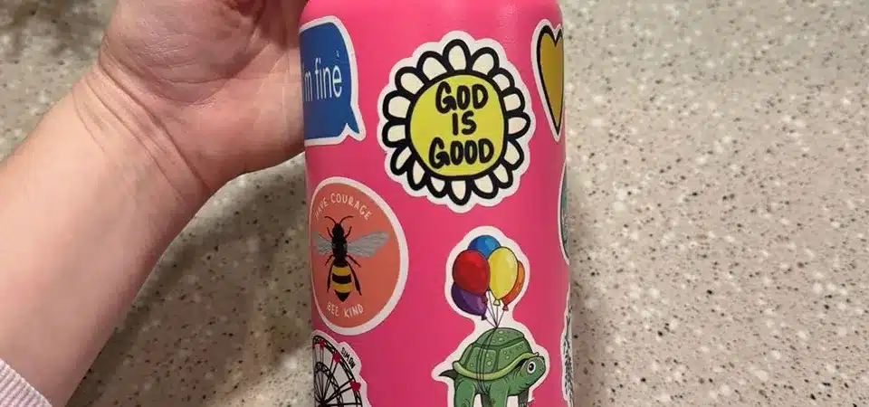 A water bottle covered in stickers being placed in the top rack of a dishwasher