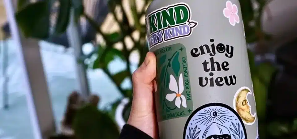 A hand firmly pressing down a laminated vinyl sticker onto the clean, smooth surface of a metal water bottle