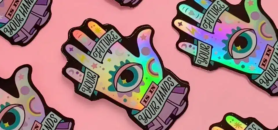 A holographic sticker showing hands holding a crystal, with holographic rays of light