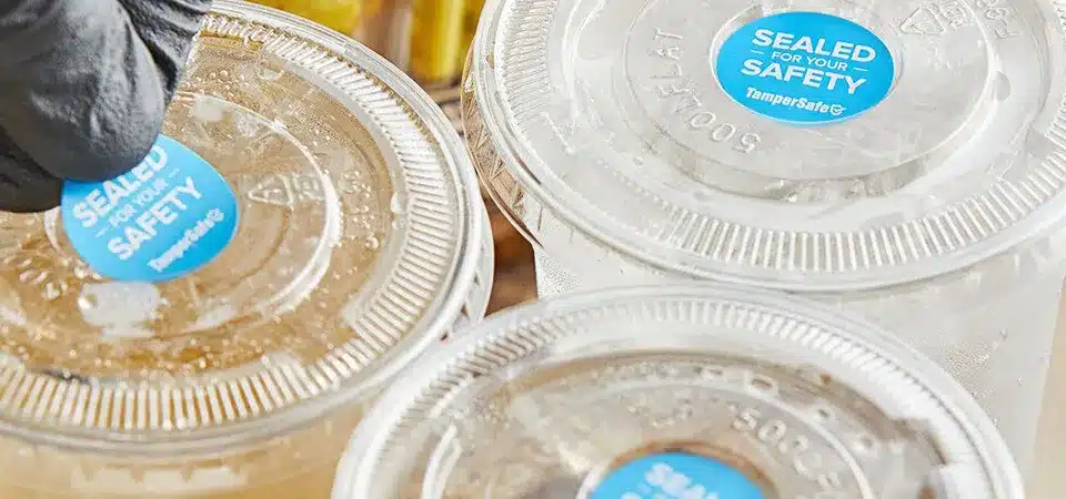 A collection of products with waterproof labels: a shampoo bottle, a cold brew coffee, and a jar of sauce