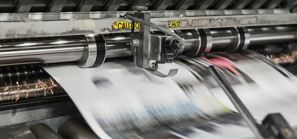 A person on a factory floor reviewing an ISO 9001 certificate with the production line in the background